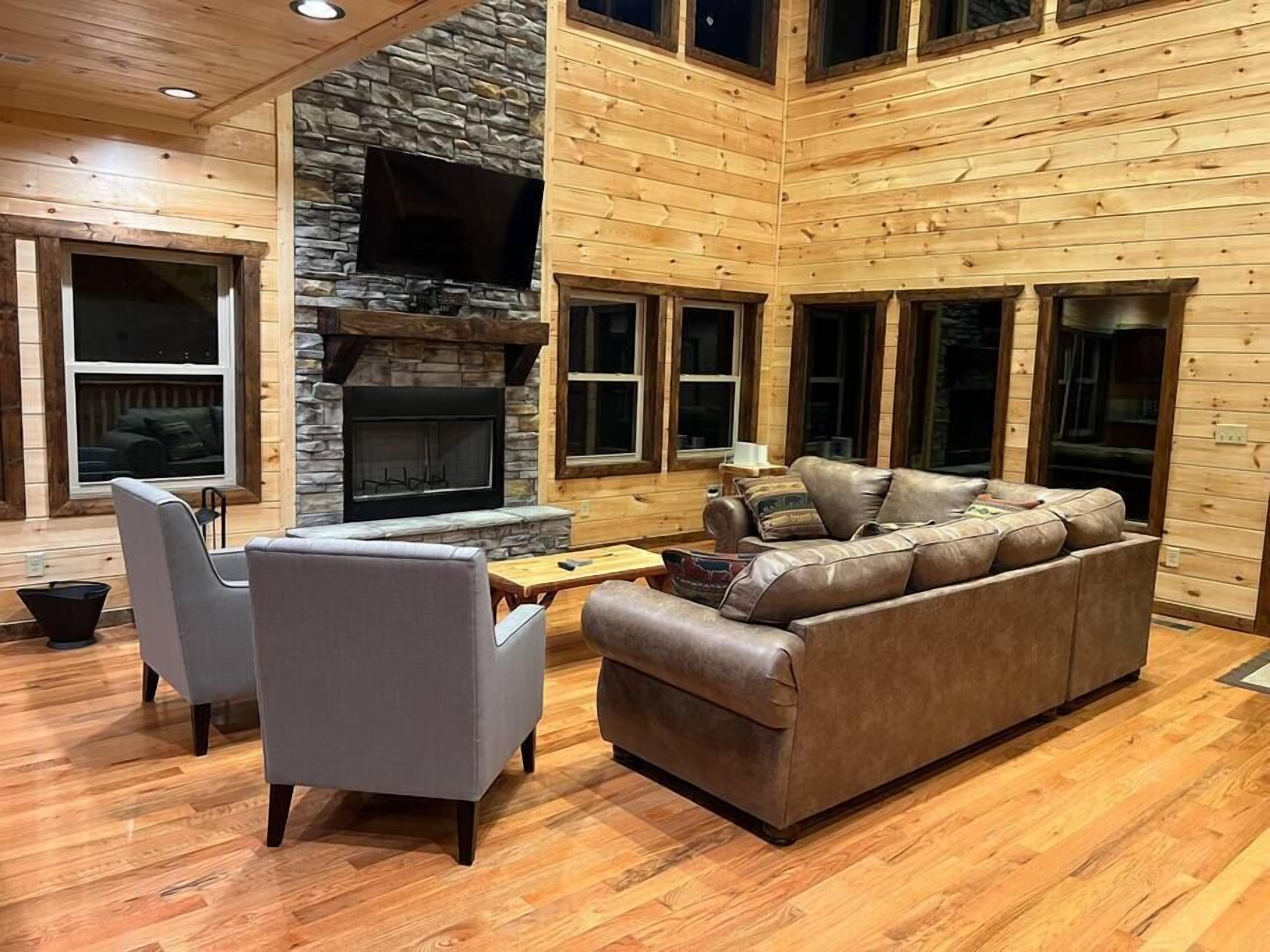 A spacious living area with a stone fireplace, wooden walls, and large windows.