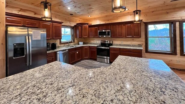 A modern kitchen with granite countertops, stainless steel appliances, wooden cabinetry, and pendant lighting. - Luxury Mtn View Cabin w/ Theater, Hot Tub, Game Room, EV Charger, Sleeps 12 (Gatlinburg)