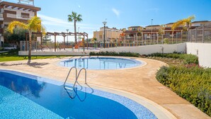 Une piscine à l’eau d’un bleu limpide, entourée d’une terrasse en béton, de palmiers et d’une clôture.