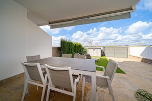 Un patio al aire libre con mesa y sillas, un área cubierta y vistas al cielo y el paisaje distante.