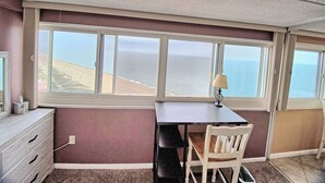 A room with a desk and chair, a lamp, a dresser, and a large window with a view of the ocean. - 🏖 *Ocean *Ocean *Ocean* 🏖 Beautiful Condo!! (Ocean City)