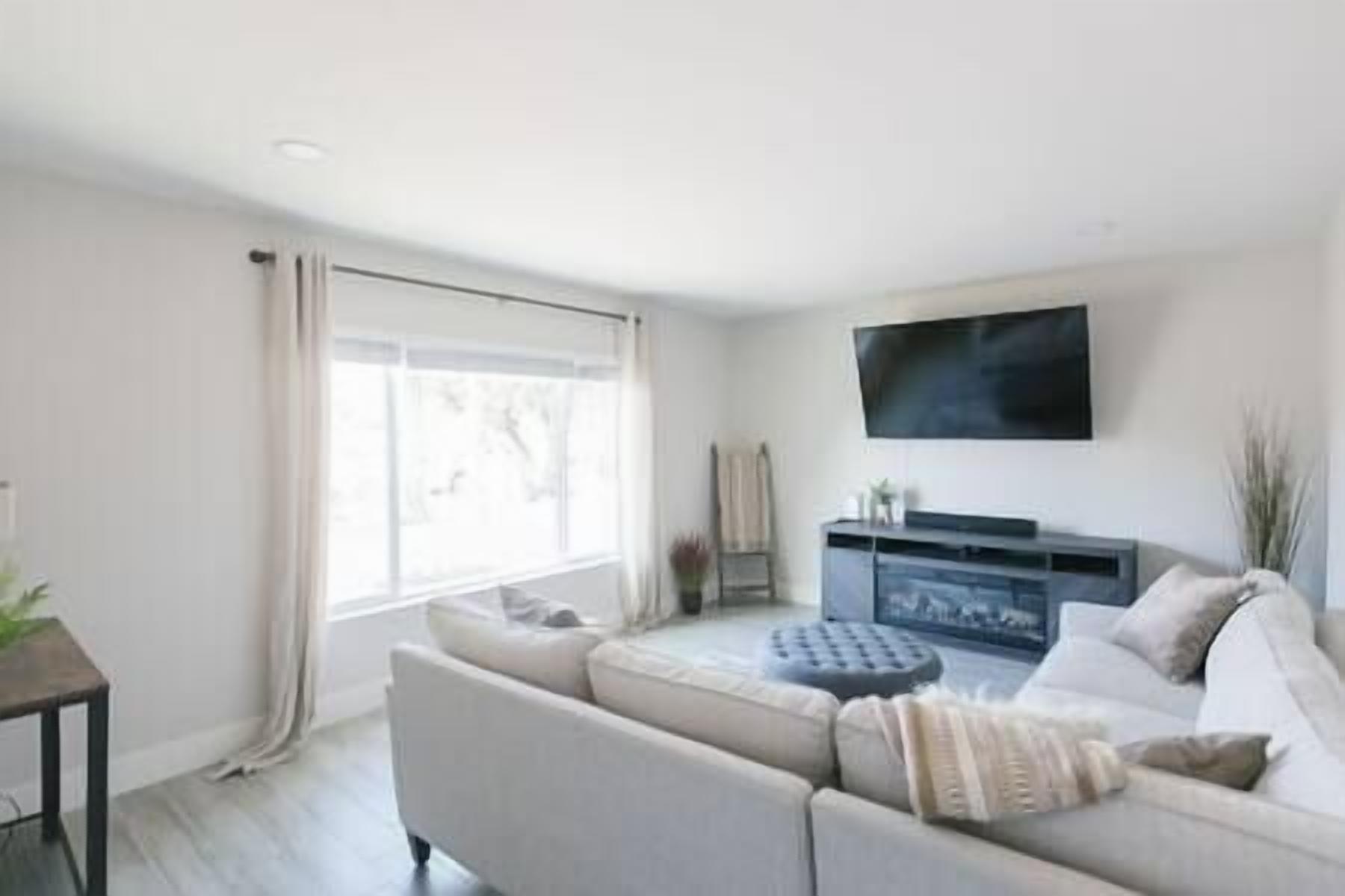 A modern living room with a sofa, a TV mounted on the wall, and a large window.