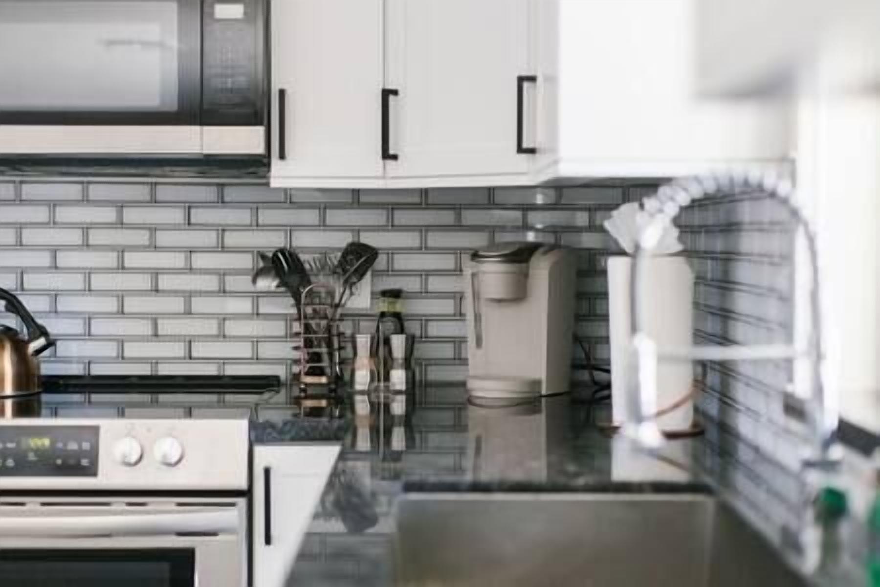 Una cocina moderna con armarios blancos, un hervidor de acero inoxidable y una cafetera.