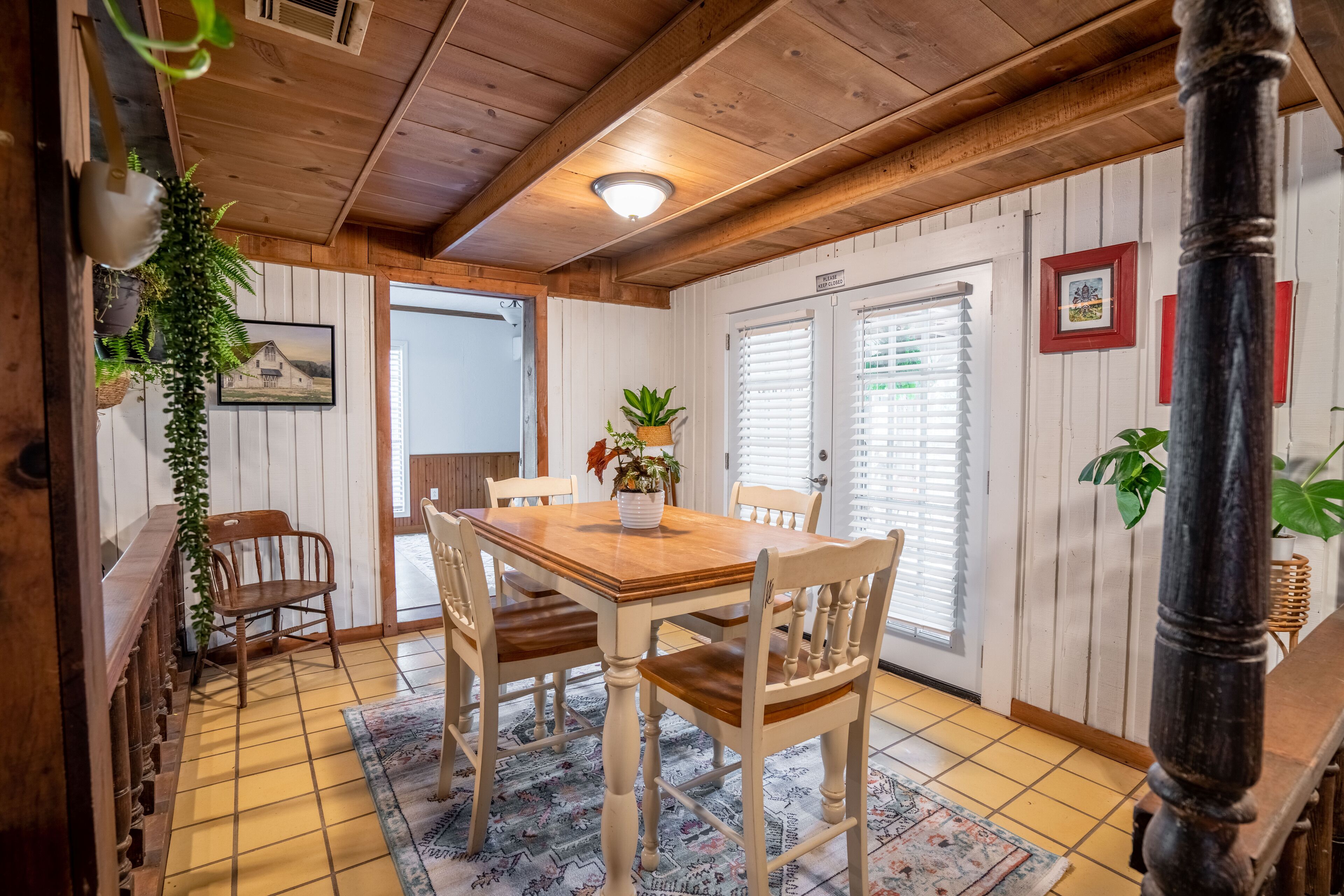 A dining area with a wooden table and chairs, a potted plant, and a view of the outside.
