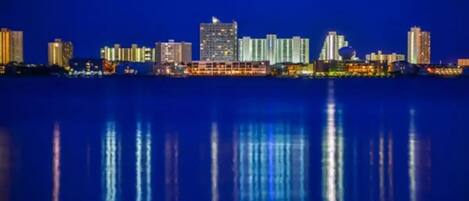 Une vue nocturne sur les grat-ciel d’une ville, les bâtiments illuminés se reflétant dans l’eau calme.
