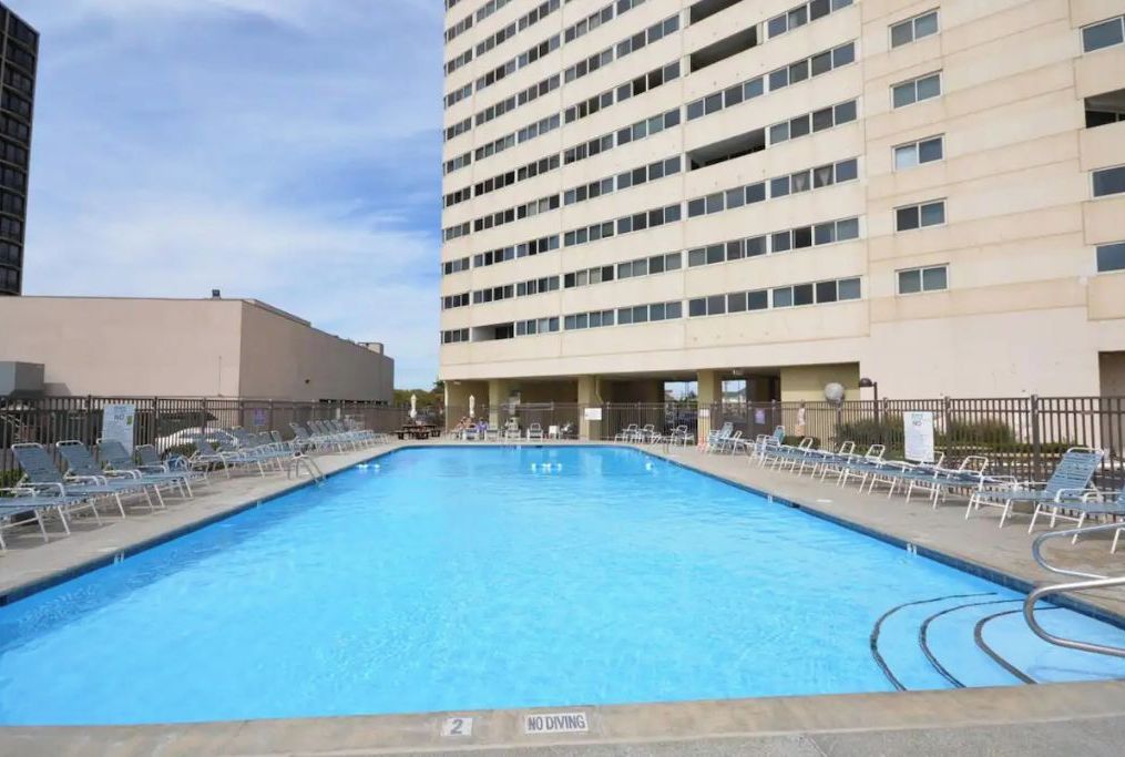 A swimming pool with lounge chairs and a 'No Diving' sign, surrounded by buildings.