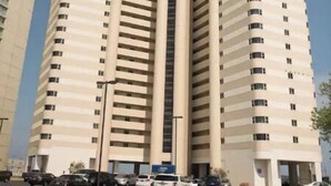 Un edificio de gran altura con varios pisos, un estacionamiento al frente y un cielo despejado.