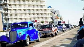 Ein blauer Oldtimer fährt auf einem Promenadenweg entlang, im Hintergrund ein mehrstöckiges Gebäude.