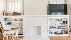 A living room with a fireplace, bookshelves, a television, and a guitar.