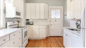 A compact kitchen with white cabinets, a microwave, a stove, and a sink.