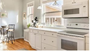 A kitchen with white cabinets, a microwave, an oven, and a window with a view of the outdoors.