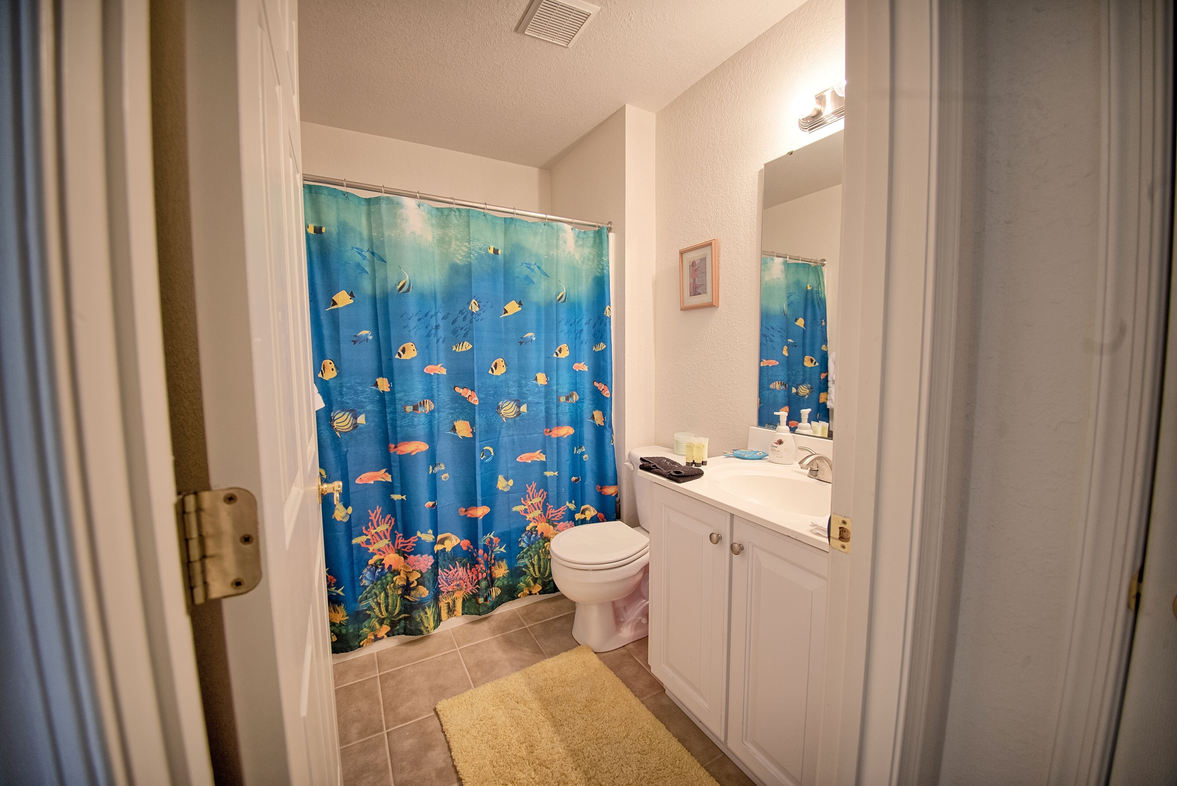 A bathroom with a shower curtain featuring an underwater scene, a toilet, a sink, and a mirror.