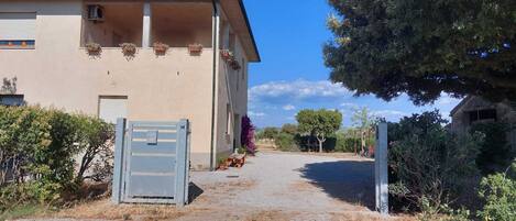 Un bâtiment avec une allée gravillonnée, un portail en métal et un arbre sur la droite.