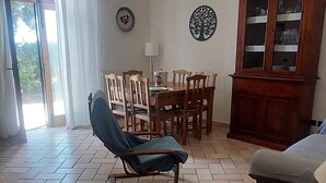 A living room with a herringbone floor pattern, a blue armchair, a wooden dining table with chairs, a cabinet with glass doors, and two wall decorations. - "Il Frassino" Farmhouse with Pool & Air Conditioning (Campiglia marittima)