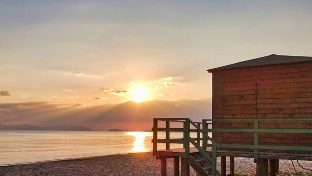A wooden structure with a staircase leading up to it, situated on a pebbled beach with the sun setting in the background. - "Il Frassino" Farmhouse with Pool & Air Conditioning (Campiglia marittima)