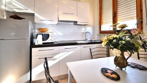 A modern kitchen with white cabinets, a stainless steel refrigerator, a microwave, and a sink. There is a dining table with a vase of flowers and a decorative plate. - "Il Frassino" Farmhouse with Pool & Air Conditioning (Campiglia marittima)