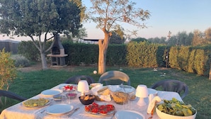 An outdoor dining setup with a table set for a meal, surrounded by chairs and a garden view. - "Il Frassino" Farmhouse with Pool & Air Conditioning (Campiglia marittima)