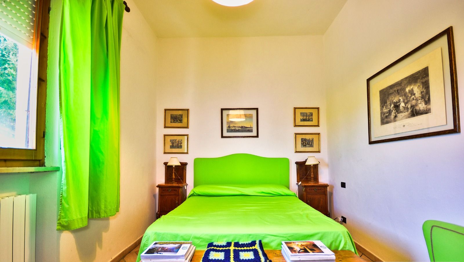 Un dormitorio con colcha verde, cabecero de madera y una mesa con libros y una manta de crochet.