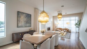 A modern living room with a dining area, featuring a large wooden table, comfortable seating, and decorative lighting. - Kirby Haus ·Modern Luxury· West U· RiceVillage · sleeps16 ·EV 🚗🔌 •3900sqft ⭐️⭐️⭐️⭐️⭐️ (Houston)