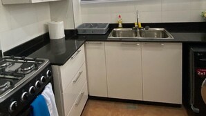 A modern kitchen with white cabinets, a black countertop, a stainless steel sink, and a gas stove. - Exotic 2 Bedrooms Apartment (Accra)