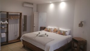 Un dormitorio con una cama de madera, un armario con ropa colgada, una mesita de noche y un aire acondicionado instalado en la pared.