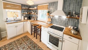 A modern kitchen with white cabinets, a wooden countertop, a built-in stove, and a window with blinds. - Gypsy Cottage · Walkable · Pet-Friendly PSJ (Port St. Joe)