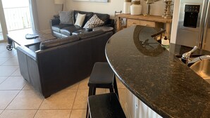 Una cocina moderna con encimera de granito curva, refrigerador de acero inoxidable y un comedor con sofá de cuero negro.