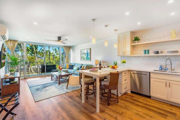 A modern kitchen with a dining area, large windows, and a view of palm trees.