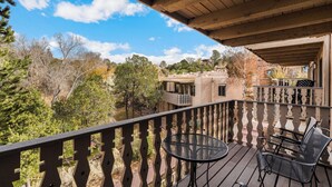 A balcony with a wooden railing, a table, and two chairs. - Fort Marcy 95 | Walk to Plaza | Kiva Fireplace | Full Kitchen | Hot Tub | Pool | End Unit | 2 Levels (Santa Fe)