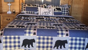 A cozy bedroom with a checkered bedspread featuring bear patterns, a wooden headboard, a bedside lamp, and a framed picture on the wall.
