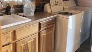 A compact kitchen with wooden cabinets, a sink, a washing machine, and a large water dispenser.