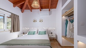 A bedroom with a bed, bedside tables, a hanging light fixture, an air conditioning unit, and a clothing rack with dresses. - Villa Christalia. Cozy family Villa 300m from the beach with swimming pool. (Κολύμπια)