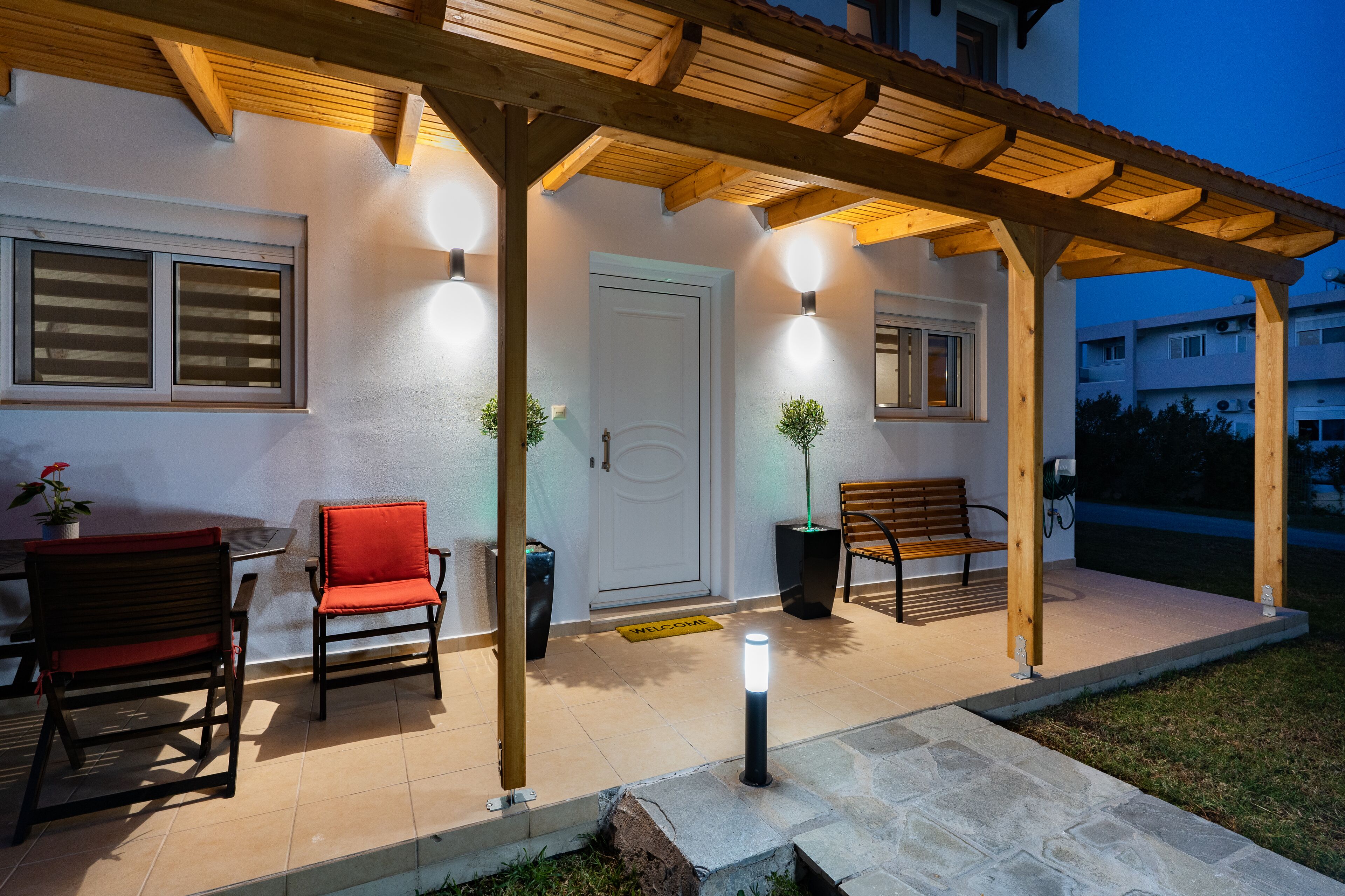 A covered outdoor seating area with a wooden pergola, a bench, and two chairs.