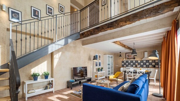 Un amplio salón con una escalera, un sofá azul, una mesa de comedor y una zona de cocina.