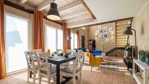 Amplia sala de estar con mesa de comedor, sillas, sofá y una escalera que lleva a un nivel superior.