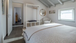 Un dormitorio con una cama grande, una silla, un armario, un espejo y una ventana.
