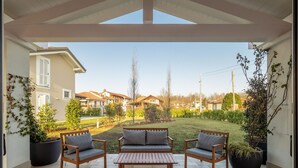 Un patio al aire libre con una mesa de madera y dos sillas, rodeado de plantas en macetas y vistas a casas vecinas.