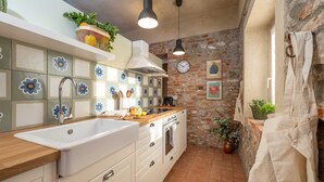 A kitchen with a white sink, wooden countertop, and a brick wall. There are hanging lights, a clock, and a plant on the wall. - Quiet Studio Apartment with Garden in Farmhouse (Cressa)