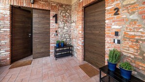 A brick-walled entrance with two dark wooden doors, numbered 1 and 2, and a small bench with potted plants. - Quiet Studio Apartment with Garden in Farmhouse (Cressa)