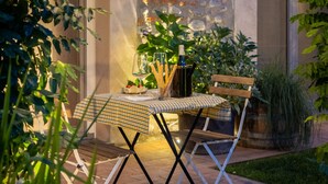 An outdoor dining area with a table set for two, surrounded by lush greenery and a stone wall. - Quiet Studio Apartment with Garden in Farmhouse (Cressa)
