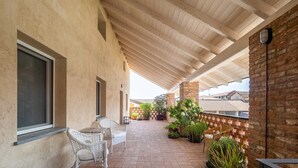Eine überdachte Terrasse mit Korbmöbeln, Topfpflanzen und einer Backsteinmauer.