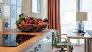 A kitchen with a fruit basket on the counter, a dining area with a table and chair, and a view of the outdoors through large windows. - One Bedroom Loft Style Apartment in Restored Farmhouse (Cressa)