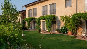 A building with a garden in front, featuring a lawn, potted plants, and a seating area. - One Bedroom Loft Style Apartment in Restored Farmhouse (Cressa)