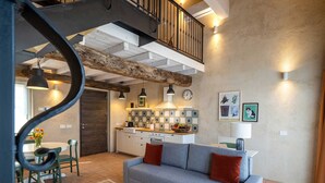A modern living room with a grey sofa, a small coffee table, and a dining area with a table and chairs. - One Bedroom Loft Style Apartment in Restored Farmhouse (Cressa)