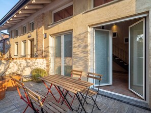 Ein modernes Haus mit einer Terrassenfläche, ausgestattet mit einem Holztisch und -stühlen, einer Treppe und großen Schiebegläsern.