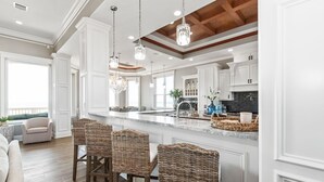 Une cuisine spacieuse dotée d’un grand îlot central, de meubles blancs et de luminaires suspendus en cristal.