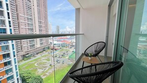 A balcony with two black chairs, a small table with a plant, and a view of a parking lot and buildings. - Accommodation with views in Costa del Este 6 (Panama)