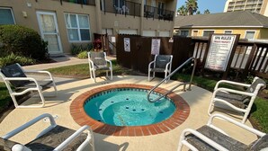 Zona de piscina con jacuzzi, rodeada de sillones de descanso, en un edificio residencial con balcones.
