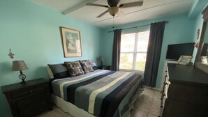Un dormitorio con cama, ventilador de techo, cómoda, televisor y ventana con cortinas.