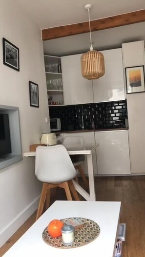 A compact kitchen with white cabinets, a black backsplash, and a hanging light fixture. - Pretty cocoon canal St Martin (Paris)